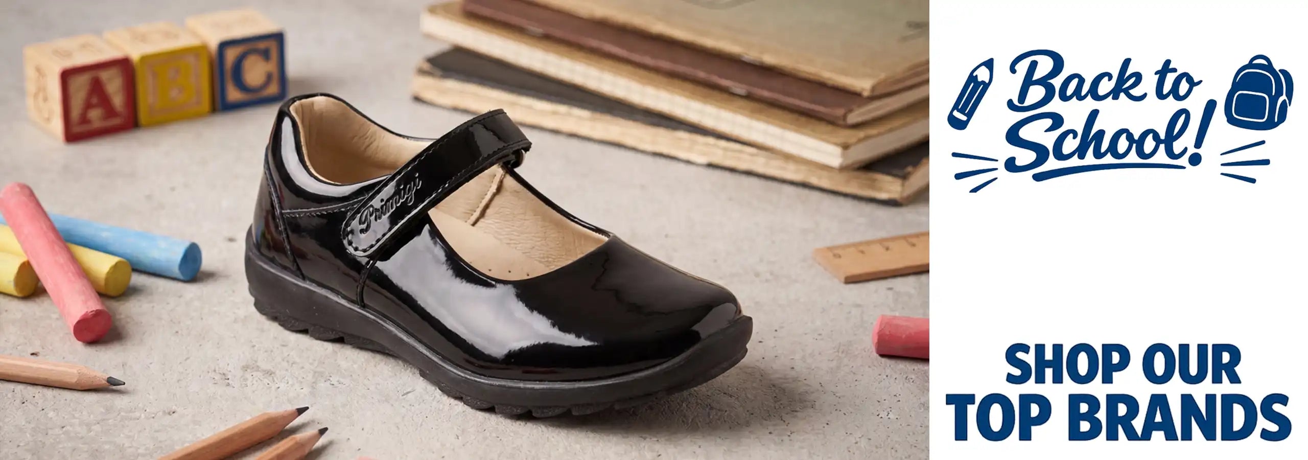 A glossy black children's Mary Jane shoe with a hook-and-loop strap, displayed on a textured surface with school-themed props like chalk, pencils, books, and blocks. The right side features a white panel with a blue 'Back to School!' graphic and the text 'SHOP OUR TOP BRANDS'.